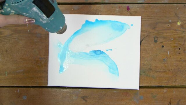 Fluid Art. Abstract pink painting. Top view of female artist uses dryer to move a blue paint and dry her new blue picture