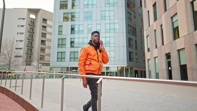 Stylish portrait of a cool black african american man in a downtown city center. He is talking on the phone. He wears bright clothes. Shot in 4k. City exploring