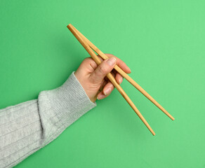 Pair of wooden chopsticks in a  female hand on a green background