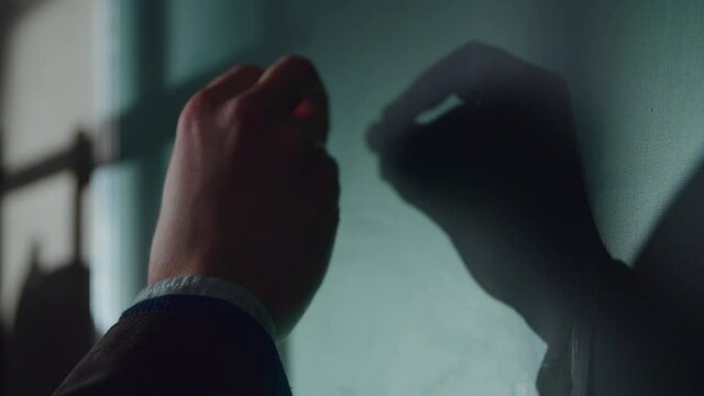 Young teacher man writes mathematical formulas using chalk on a green school chalkboard