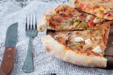 Closeup photo of mixed pizza slices on wooden board with fork and knife