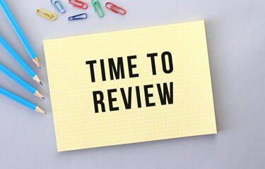 TIME TO REVIEW text in notebook on gray background next to pencils and paper clips.