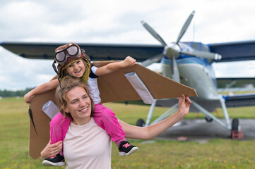 A Caucasian woman and her little daughter are playing a pilot against the backdrop of a small plane with a propeller © Михаил Решетников