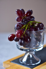 Dark purple grapes in a glass goblet on a slate and bamboo stand.