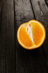 Half a fresh orange on a black wooden background. Free space, fruit.