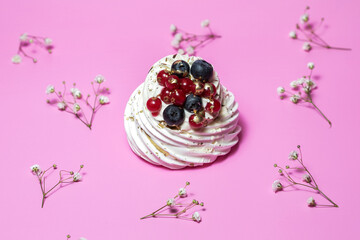 Meringue dessert with blueberries and currants on pink background