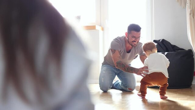 Happy father helping little son walking in living room
