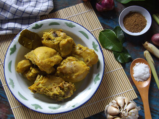 Image of ayam ungkep bumbu kuning with ingredients around. Chicken cooked with herbs and spices such as turmeric, lemon grass, garlic, coriander, ginger, lime leaves, candle nuts. Ready to be fried. 