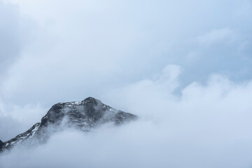Epic Winter landscape image of view from Side Pike towards Langdale pikes with low level clouds on mountain tops and moody mist swirling around