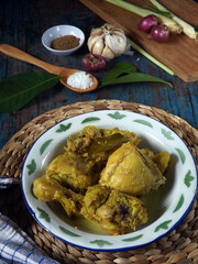 Image of ayam ungkep bumbu kuning with ingredients around. Chicken cooked with herbs and spices such as turmeric, lemon grass, garlic, coriander, ginger, lime leaves, candle nuts. Ready to be fried. 