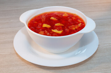 Borscht soup with meat in a white bowl on a wooden table.