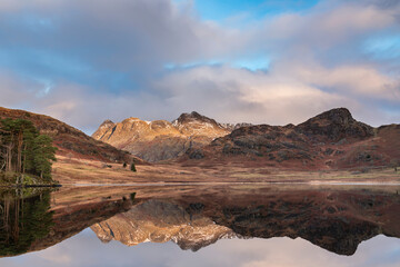 Fototapeta na wymiar Beautiful vibrant Winter sunrise over Blea Tarn in Lake District with snow capped Langdale Pikes in distance