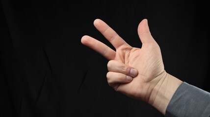 Men's hand gesturing, gesture, enumeration three, three fingers, isolated black background. Emotion