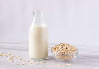 Vegetable oat milk in a glass bottle and oat flakes on a light background. Healthy drinks, vegetarianism. Side view