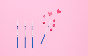 Negative and positive pregnancy test strip and red hearts on a pink background, top view. Waiting for the birth of a child