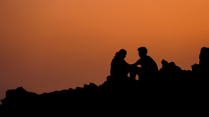Fototapeta na wymiar A couple sitting on the rock silhouette