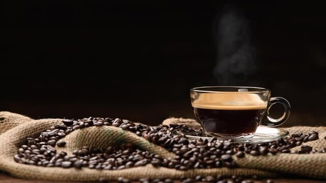 Cup glass of coffee with smoke and coffee beans on burlap sack on old wooden background