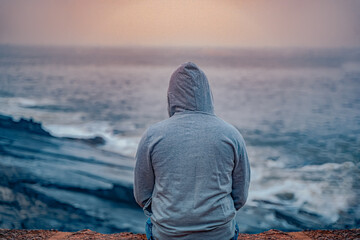 Anonymous guy sitting near seashore wearing grey hoodie