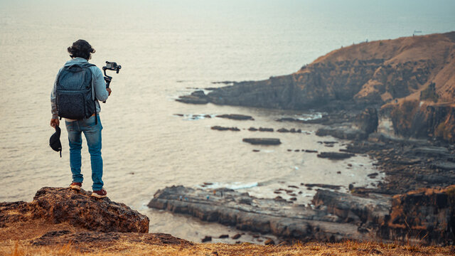 Independent filmmaker standing on the cliff holding camera in his hand
