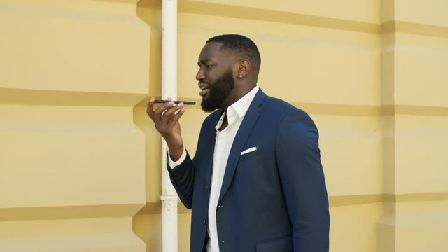 Sad businessman talking on speakerphone outside. Afro man walking outdoors