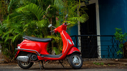 Red scooter parked against green background at the street - obrazy, fototapety, plakaty