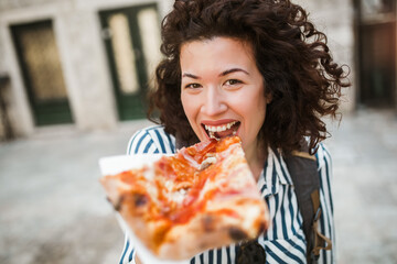 Beautiful young curly hair woman eating a slice of pizza outdoor.