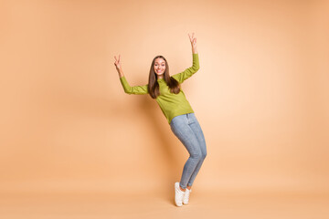 Fototapeta na wymiar Full length photo of lady tiptoes show two v-signs wear green pullover footwear jeans isolated beige color background
