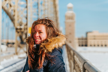 A young woman in a jacket walks on a snow bridge in St. Petersburg in winter in sunny weather