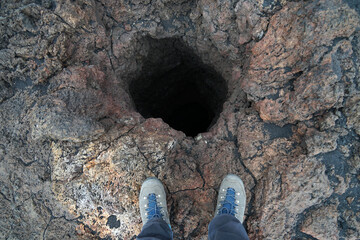 Hiker standing above dangerous deep volcanic hole cave in ground, guided tour hiking concept on...