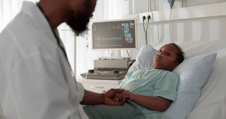 African child lying in bed in hospital room with doctor comforting her and holding hand