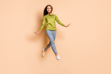 Fototapeta na wymiar Full length body size view of pretty funny cheerful girl jumping strolling having fun isolated over beige pastel color background