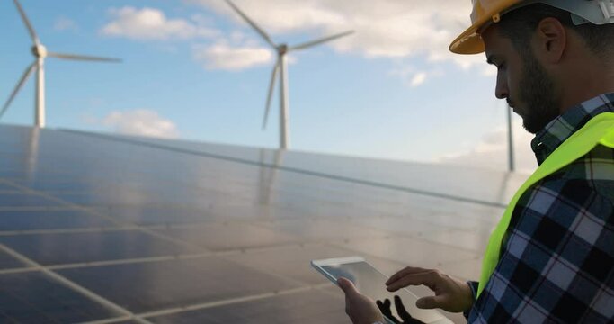 Young man working with digital tablet - Solar panels with wind turbines generating electricity - Alternative renewable energy from nature - Ecology concept