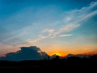Orange sun is setting behind the mountains, clouds in the blue sky, empty space, no people.