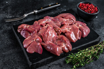 Raw chicken liver meat on marble board with thyme. Black background. Top view