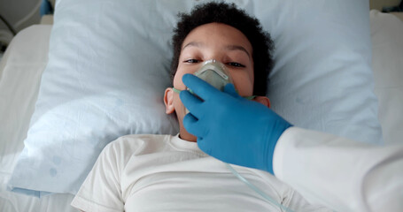 Nurse putting oxygen mask on african patient child in hospital bed