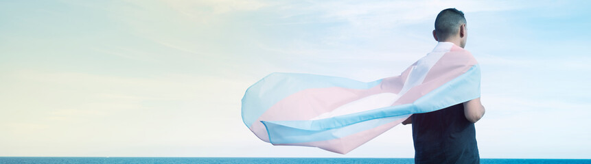 person wrapped in a transgender flag, web banner - obrazy, fototapety, plakaty