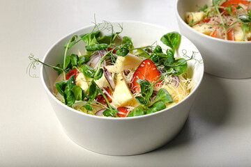 Close-up fruit salad with strawberries, pineapple pieces, herbs, red onions and cheese in white ceramic bowls on a light background. Ideas and recipes for a healthy diet. Organic nutrition