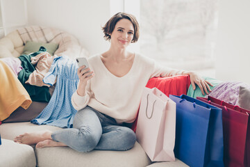 Full length photo of bob haired pretty woman sit sofa hold smartphone remote shopping bags indoors in house