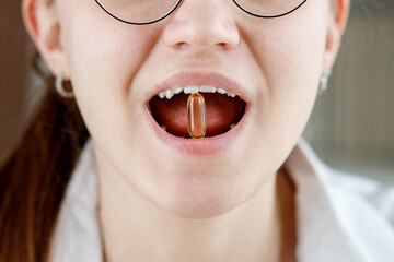 The girl holds in her mouth a capsule of fish oil.