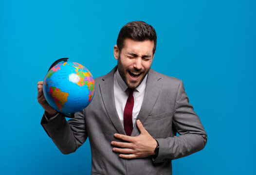 young businessman laughing out loud at some hilarious joke, feeling happy and cheerful, having fun holding a world globe map
