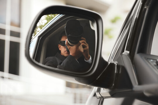 Private detective with camera spying from auto, view through car side mirror