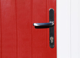 A closeup view of a grey brushed chrome handle on a red door.