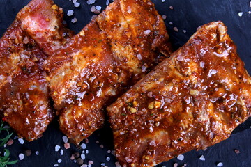Raw marinated pork ribs on black stone plate ready for cooking. Raw bbq ribs, marinated meat for grill, meat with bone