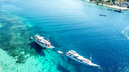 Top down drone shot of two boats anchored in one of the bays of Komodo National Park, Flores, Indonesia. The sea is crystal clear, shining with turquoise and blue shades. Island hoping