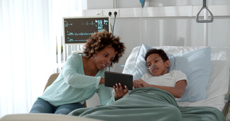 Happy mixed race mother and son using digital tablet in ward at hospital