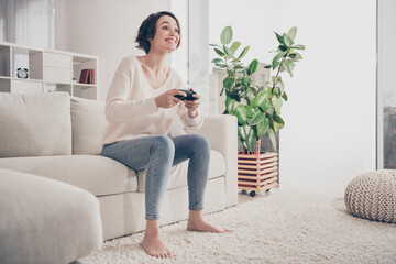 Full length portrait of cheerful carefree young girl sit on sofa look interested arms hold game pad toothy smile indoors