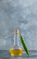 Vertical photo of hot pepper with bottle of oil on grey background