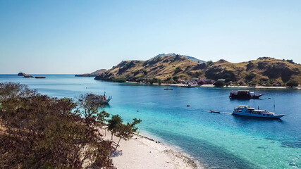 Fototapeta na wymiar Top down drone shot of a paradise island with some boats anchored around in Komodo National Park, Flores, Indonesia. Brownish island turns into white sand beach and further into green and navy sea