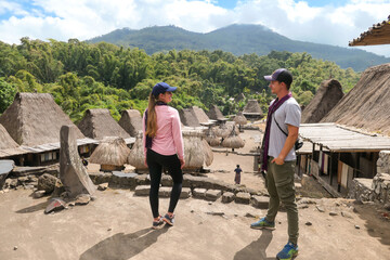Fototapeta na wymiar A couple with a purple scarfs admiring the Beno village in Flores, Indonesia. There are many small houses behind him. Each house is made of natural parts like wood and straw. History and tradition