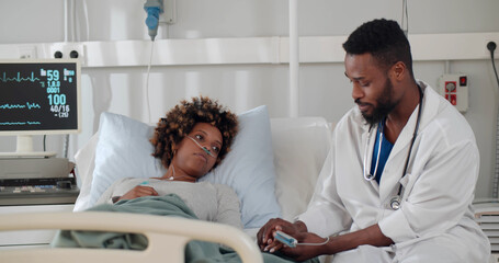 Doctor talking about treatment to afro female patient in hospital ward